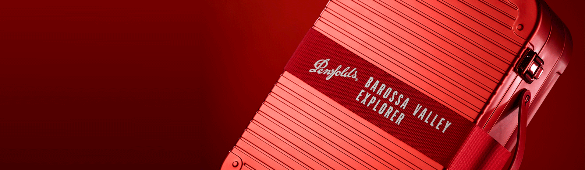 Close up of red luggage tin with material belt close against red background. 'Penfolds Barossa Valley Explorer' is written across the belt
