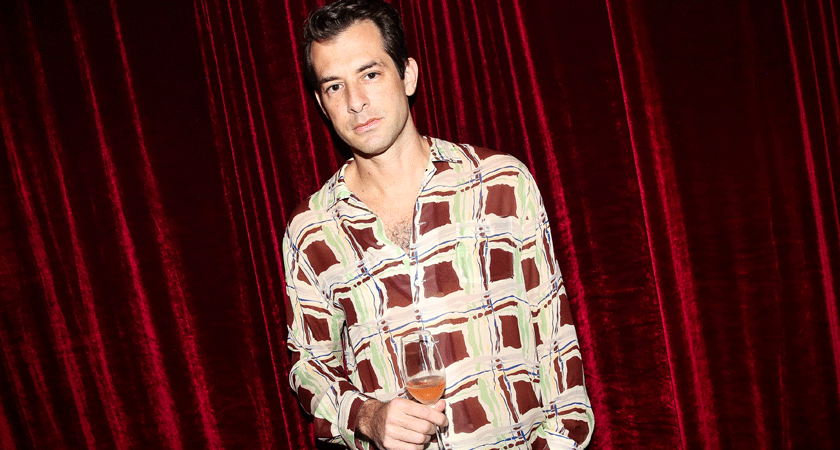 Mark Ronson poses with a glass of rose in front of a red velvet curtain