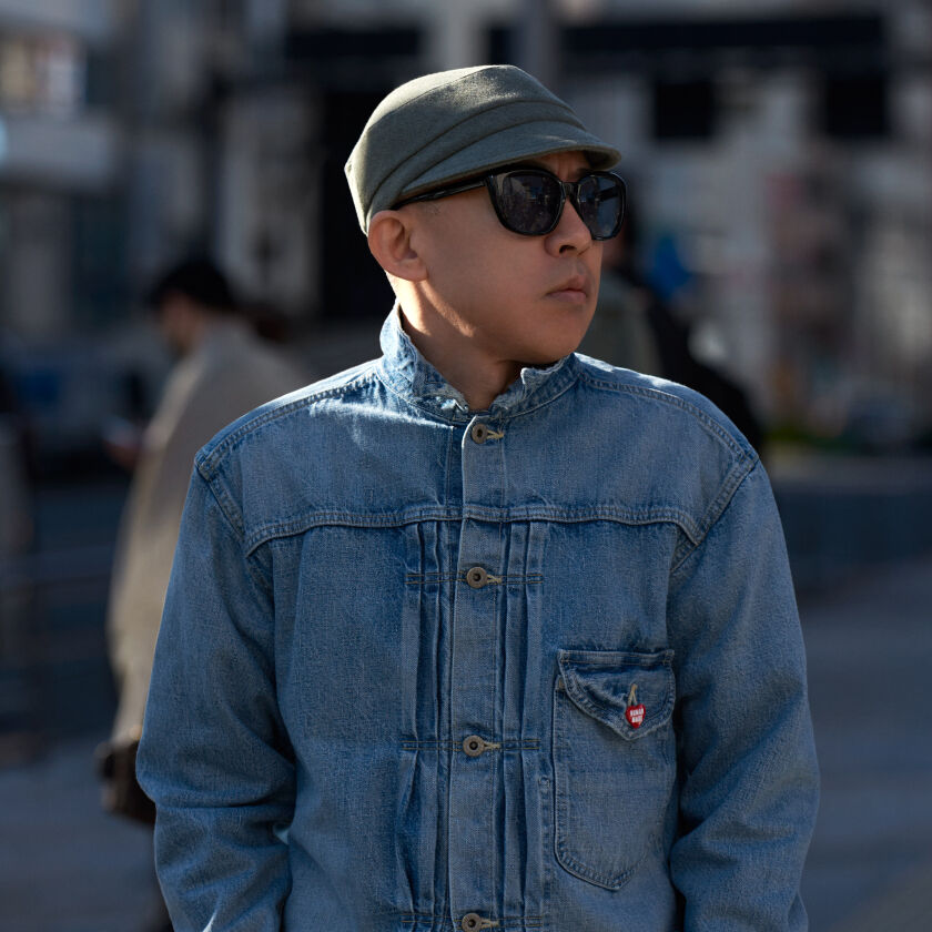 Nigo stands in blue denim jacket in the middle of a city street.