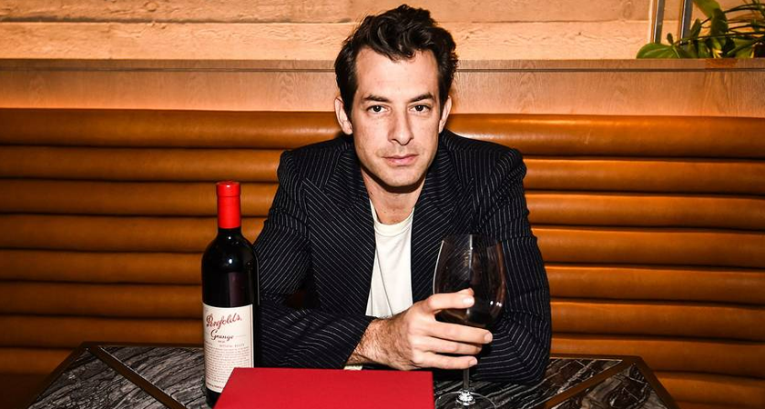 Mark Ronson sits at table with a glass of red wine in hand.  Grange bottle sits on the table.