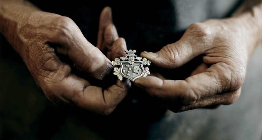 Handcrafted metal crest being held by two weathered hands