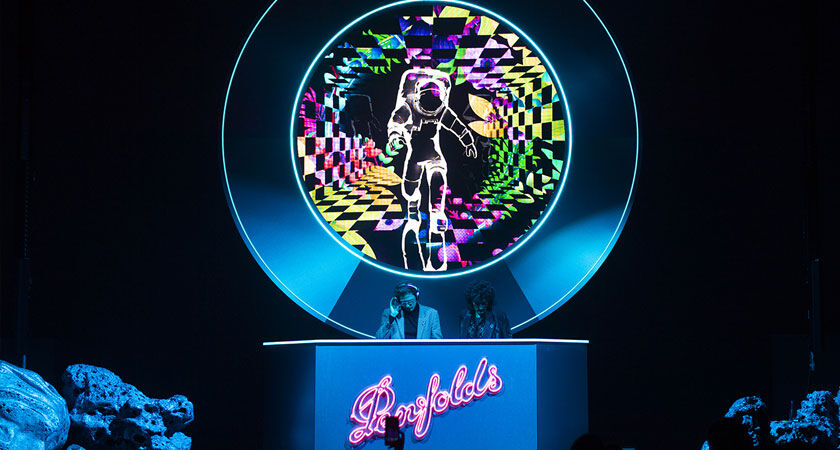 Two DJs perform on stage with neon astronaut projection behind