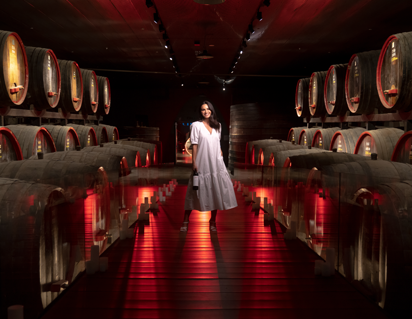 Lady in white dress stands in barrel hall of Magill Estate