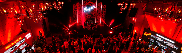 Overhead shot of event with red lighting.  people mingle in front of a stage..