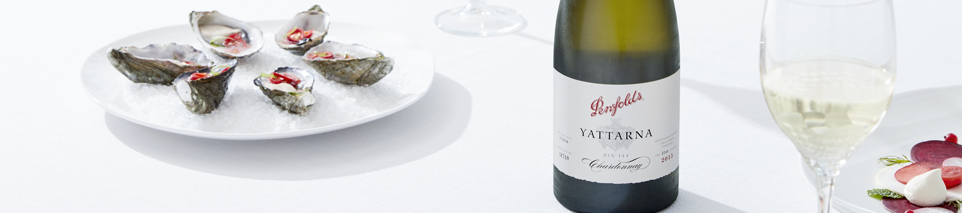 Bottle of Yattarna Chardonnay centred on a white tablecloth.  A glass to the right and a plate of oysters to the left.