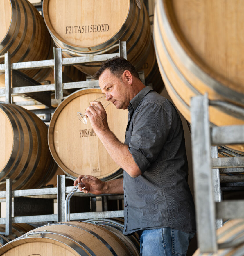 Kym Schroeter, Penfolds White Winemaker, sniffing wine in front of barrels. 