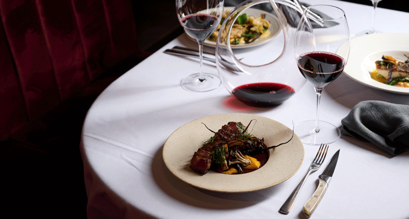 Steak dish on white table cloth with two glasses of red wine