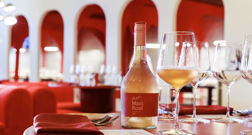 Max's Rosé sits on ta red table with white arch walk ways behind 