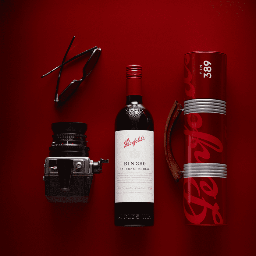Flat lay of Bin 389 bottle, gift tin, camera and sunglasses