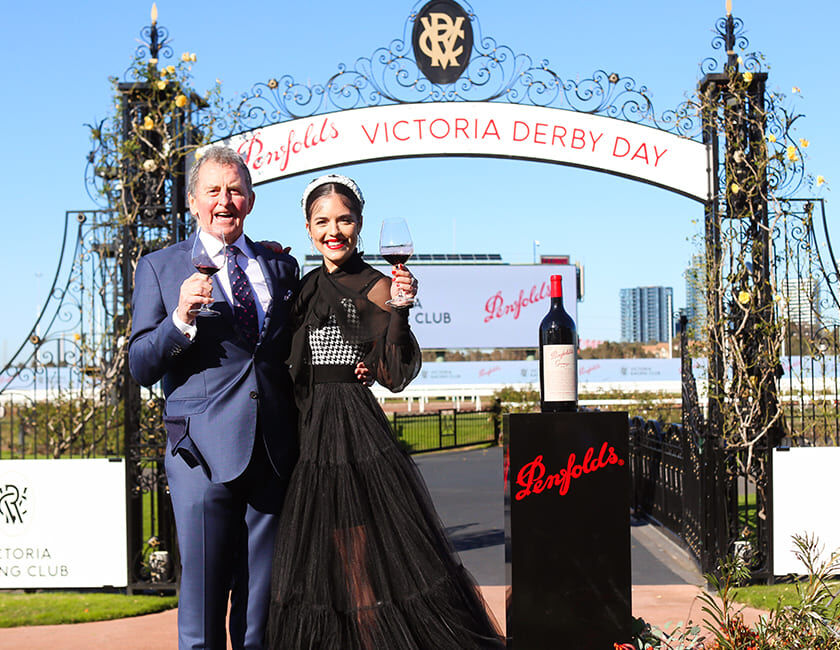 Two people stand on the racetrack in front of Penfolds Derby Day sign