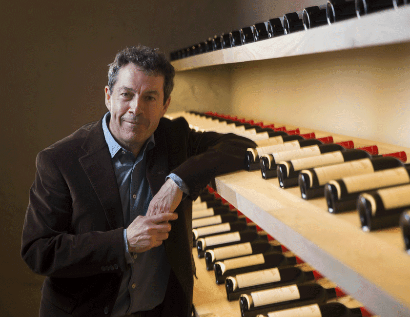 Peter Gago, Chief Winemaker, stands with elbow resting on a shelf of wine bottles