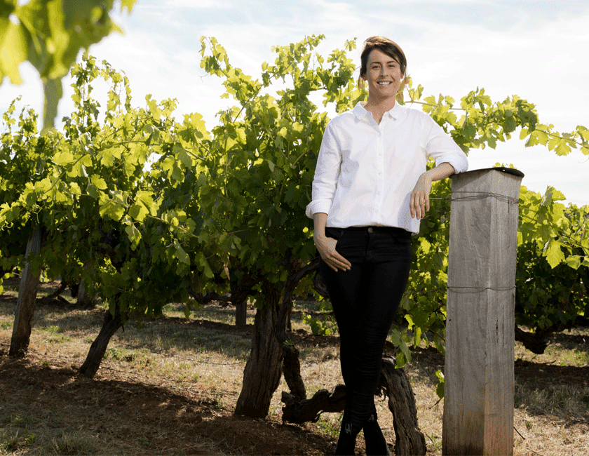 Steph Dutton stands at the end of a row of vines 