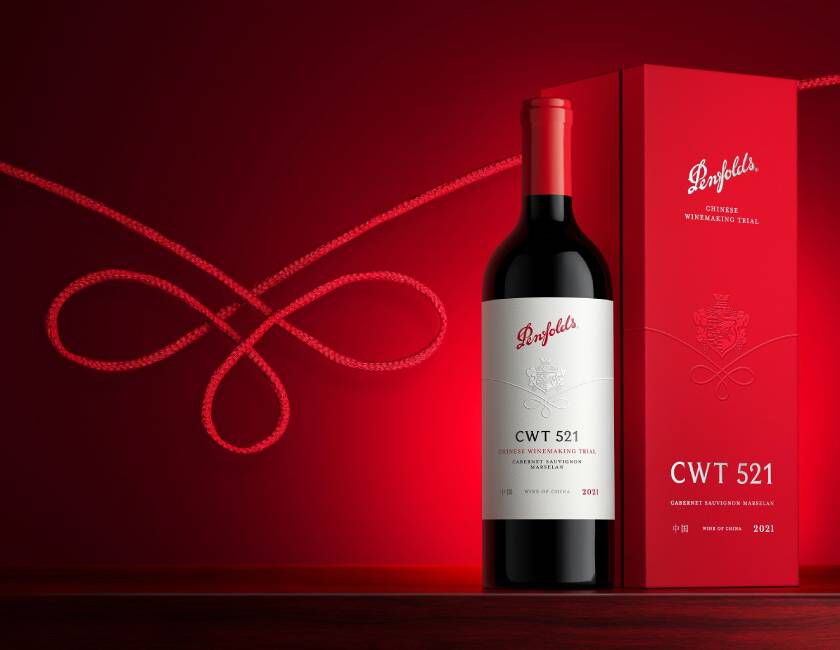 Bottle of Penfolds CWT stands against red decorative background alongside red wine box. 