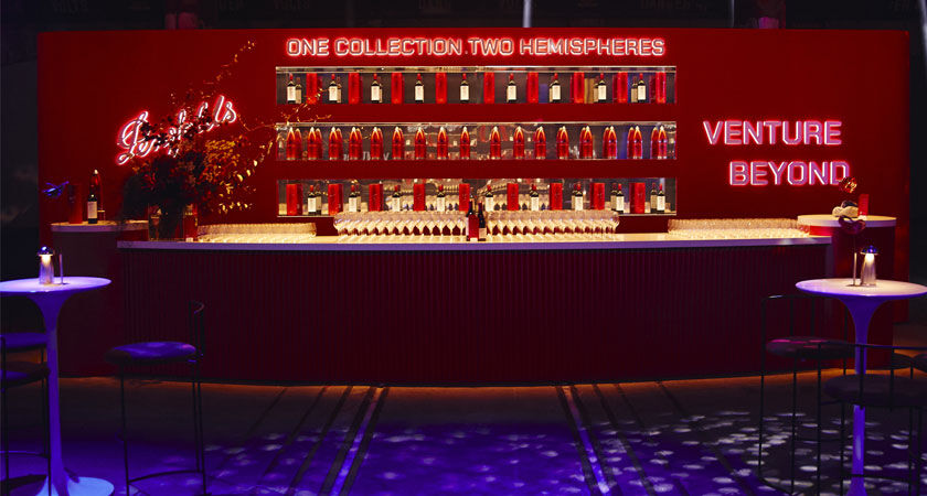 Front view of red bar at event. Wine bottles are displayed behind and 'two hemispheres. one collection' is written across the top in neon lights