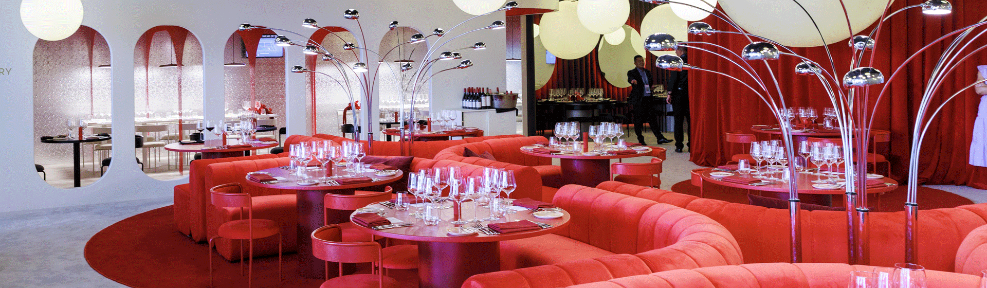 View across Penfolds x Australian Open pop-up restaurant.  3-4 round tables with round red velvet couches, round rugs and hanging lights.