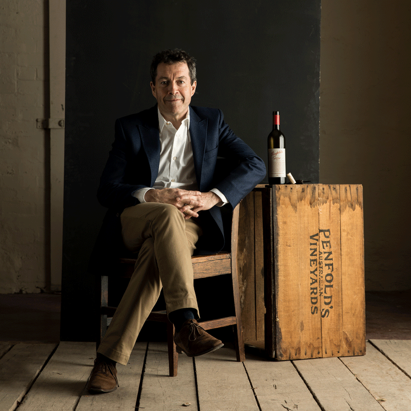 Peter Gago, Penfolds Chief Winemaker, sits inside on a chair facing the camera.  A bottle of Grange sits beside him on a wooden Penfolds crate. 