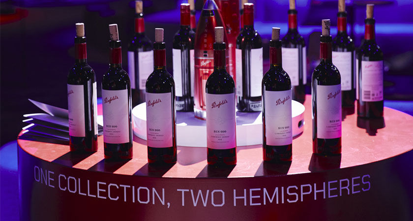 Penfolds wine bottles on a round red table.  Text around the table reads 'Two Hemispheres. One Collection'