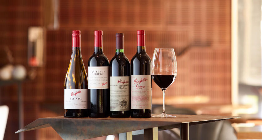 Four bottles of Penfolds wines stand on a cast iron table alongside a glass of red wine. 