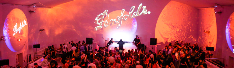 Overhead shot of event with red and orange lighting.  people mingle in front of a stage..