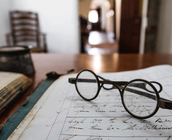 Vintage glasses rest on handwritten notes on an old desk